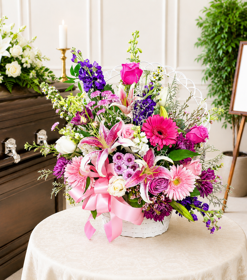 Deluxe funeral wicker basket arrangement displayed on a table at a funeral service featuring fresh seasonal flowers by Wendys Flowers in Gilbertsville, PA.