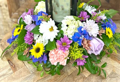 Keepsake memorial lantern displayed within a handcrafted fresh flower arrangement featuring roses, hydrangeas, daisies, and seasonal blooms, offering a thoughtful sympathy gift that provides lasting remembrance and comfort.